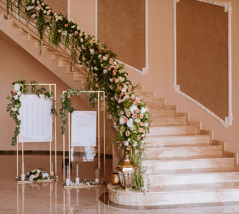 Stillvoller Gästeempfang für eine Veranstaltung oder Hochzeit mit Willkommenstafel und Bestuhlungsplan. Foyer mit Marmortreppe traumhaft dekoriert mit Blumen und Kerzen in lachs und weiß.