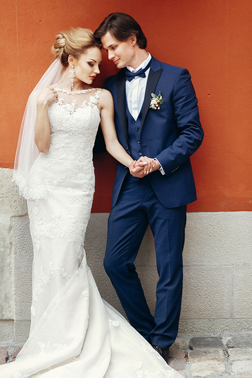 Luxury Wedding in Rom. Frisch vermähltes Hochzeitspaar posiert Hände haltend an einer terracottafarbenen Wand im Freien in der Stadt. Hochzeitskonzept in blau-orange.