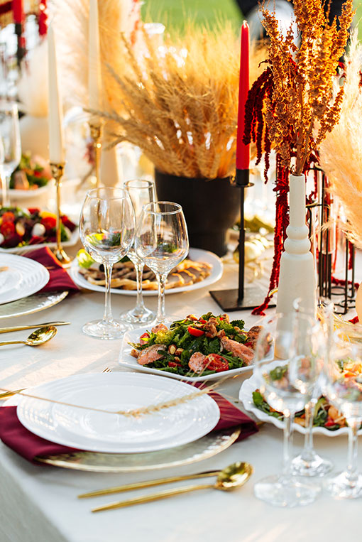 Festlich dekorierte Tafel mit elegantem Tischgedeck, goldenem Besteck und herbstlichen Trockenblumen in Rottönen