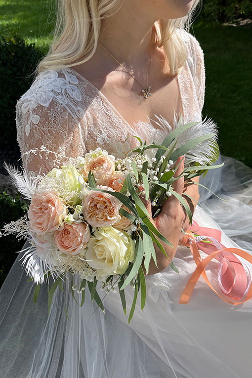 Braut sitzt im Garten und hält ihren Brautstrauss im Arm. Schöner romantischer Moment.